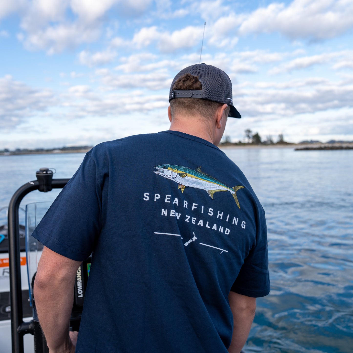 Person on a boat wearing a navy blue t-shirt with 'Spearfishing New Zealand' text and fish illustration.