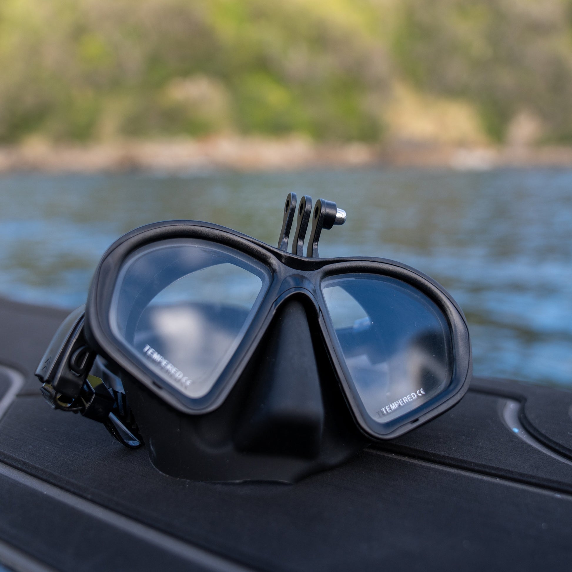 Black diving mask with GoPro on a boat's dashboard by a body of water