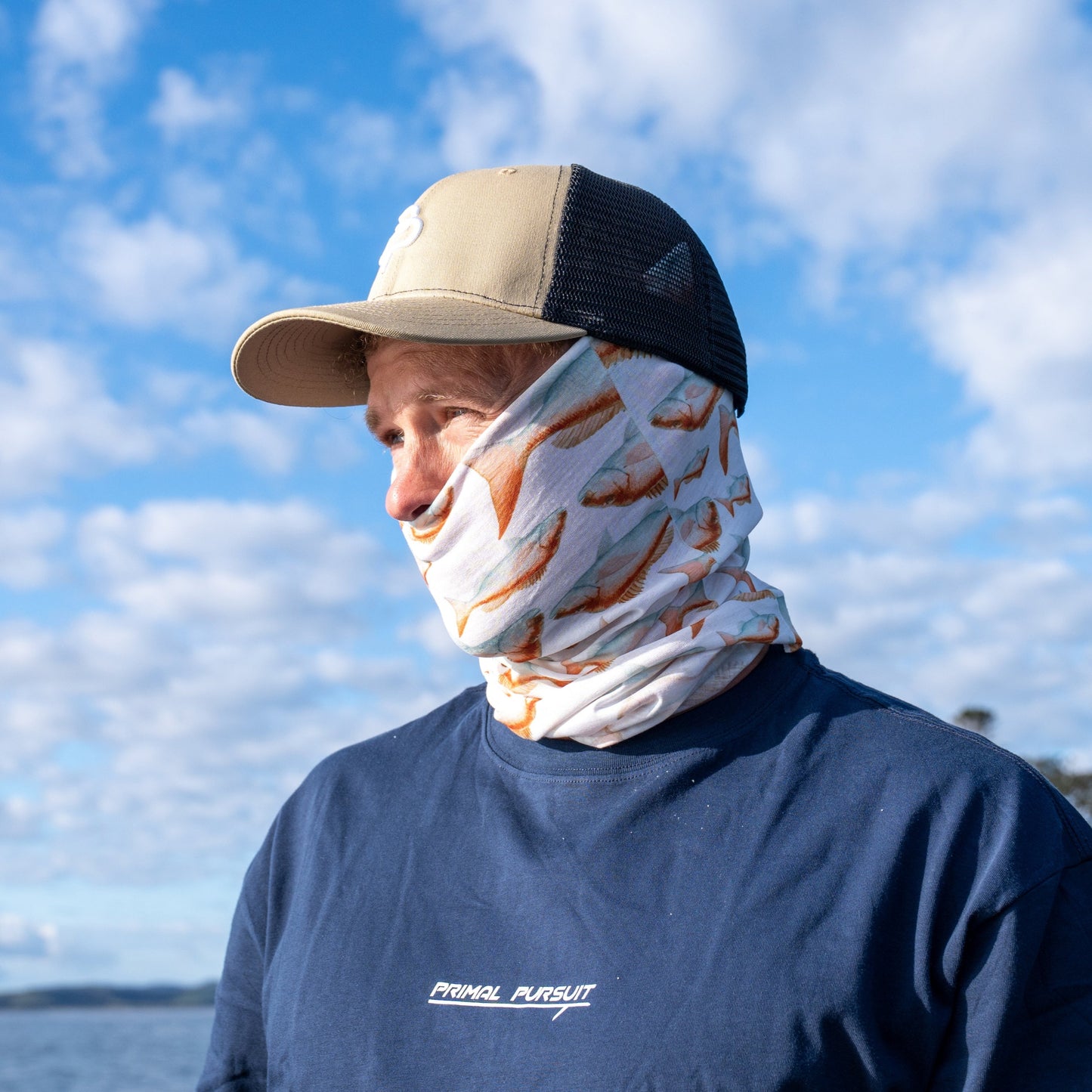 Person wearing a face mask and cap outdoors with a blue sky and water background
