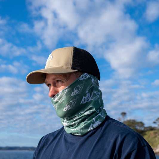 Person wearing a cap and green patterned face cover against a blue sky with clouds