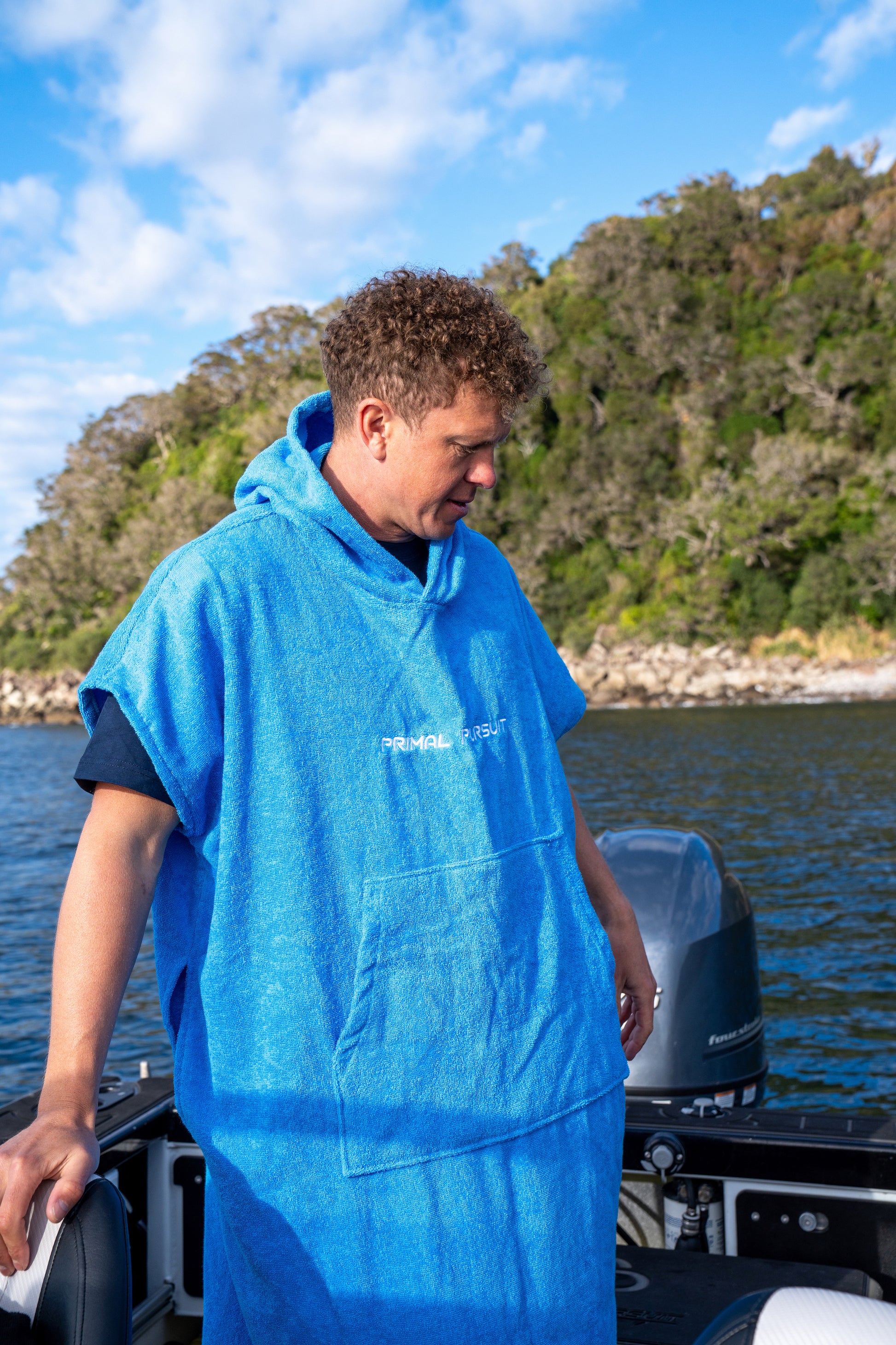 Person wearing a blue poncho on a boat with a scenic background