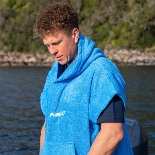 Person wearing a blue poncho with a logo, standing on a boat by water.