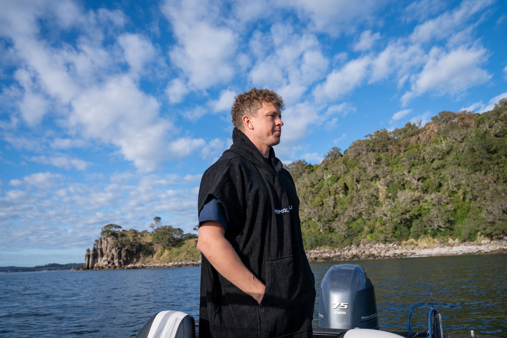 Person standing on a boat with a scenic background of water and hills.